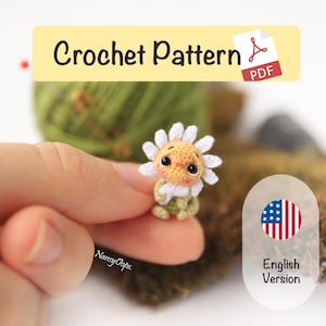 May include: A crocheted daisy doll with a smiling face, white petals, and green leaves. The image includes the text "Crochet Pattern PDF" and "English Version". The doll is held in a person's hand.