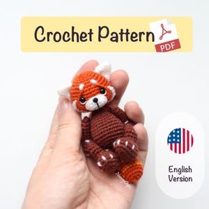 May include: A small, crocheted red panda toy with a brown body, orange head, and white details. The image shows the text "Crochet Pattern PDF" and "English Version". The toy is held in a hand.