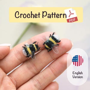 Può includere: Due api all'uncinetto fatte a mano con dettagli neri, gialli e bianchi, tenute in una mano. Le api hanno ali trasparenti. L'immagine include il testo "Crochet Pattern PDF" e "English Version".