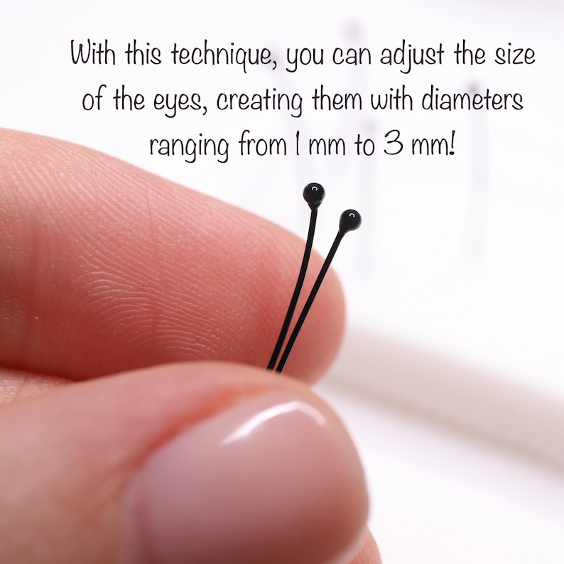 May include: Close-up of two black-headed pins with the text: "With this technique, you can adjust the size of the eyes, creating them with diameters ranging from 1 mm to 3 mm!" These pins are likely used for crafting or doll making.