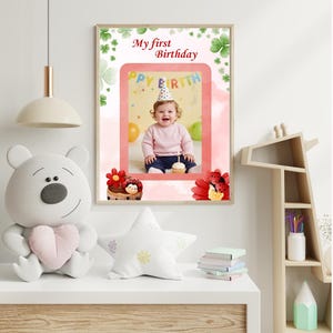 May include: A framed photo with the text "My first Birthday" features a baby wearing a party hat. The photo is surrounded by a pink border and decorative elements. A plush bear and star-shaped pillow are on a white surface.