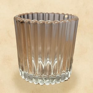 以下が含まれることがあります： 透明なリブ付きガラスの奉納キャンドルホルダー。ガラスはテクスチャード加工された垂直パターンとスカラップの縁があります。キャンドルホルダーは小さなキャンドルを保持するように設計されており、家の装飾に適しています。