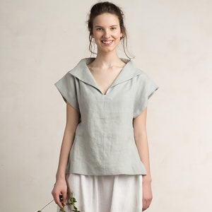 May include: A light blue linen top with a wide, folded collar and short sleeves. The top has a v-neckline and a relaxed fit.