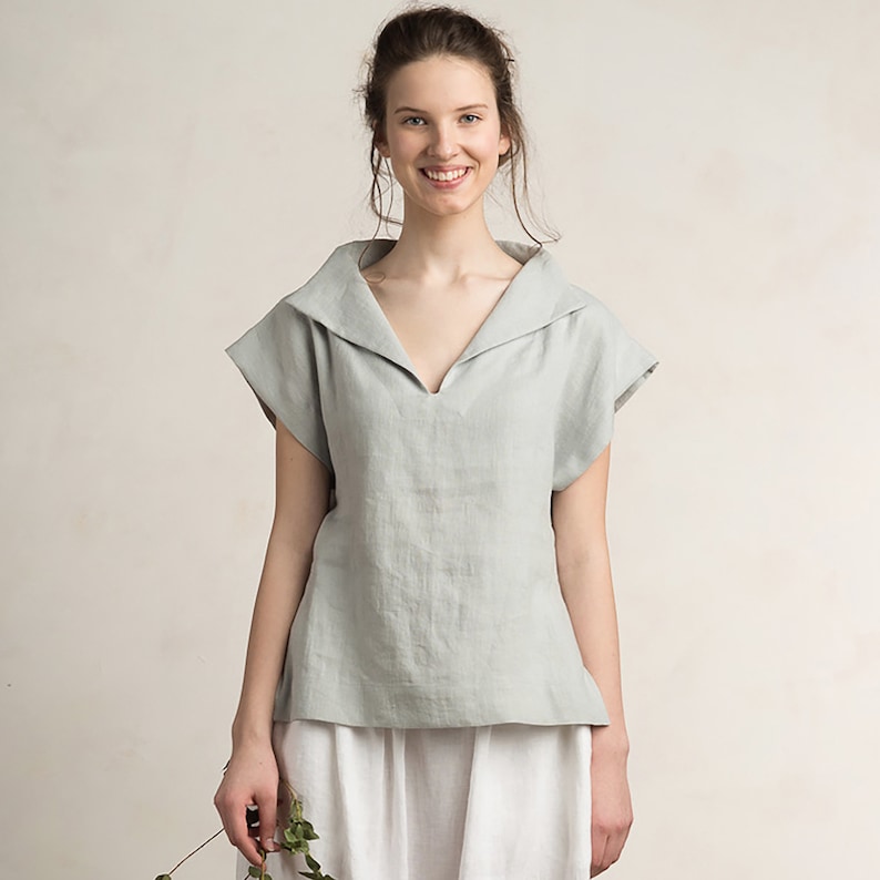 May include: A light blue linen top with a wide, folded collar and short sleeves. The top has a v-neckline and a relaxed fit.