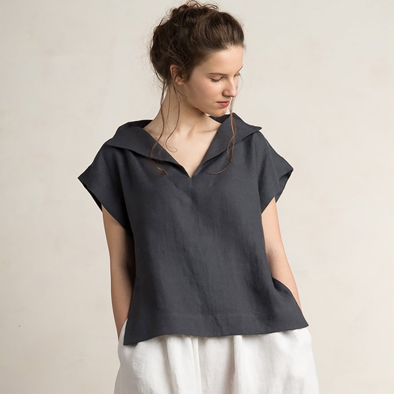 May include: A dark gray linen shirt with a wide, sailor-style collar and short sleeves. The shirt has a relaxed fit and a slightly cropped length.