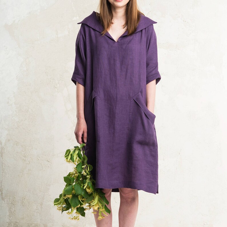 May include: A purple linen dress with a wide collar and pockets. The dress is knee-length and has a relaxed fit.