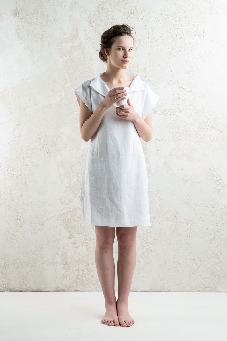May include: A white linen dress with a wide collar and short sleeves. The dress is knee-length and has a relaxed fit.