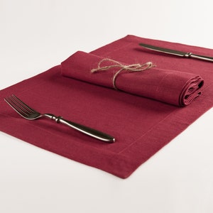 May include: A red linen placemat with a rolled linen napkin tied with twine and a silver fork on top.