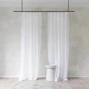 May include: White sheer curtains hanging from a black rod against a white wall. A white stool is in the centre of the image.