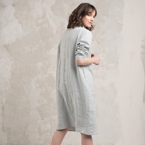 May include: A light grey linen dress with a long sleeve and a slightly A-line silhouette.