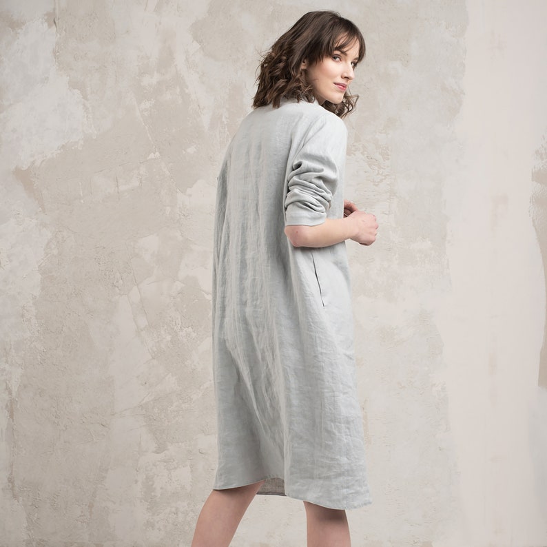 May include: A light grey linen dress with a long sleeve and a slightly A-line silhouette.