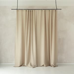 May include: Beige-colored curtain panels hanging from a black rod and chain. The curtains are made of a soft, flowing fabric and are gathered at the top. The background is a light beige wall.