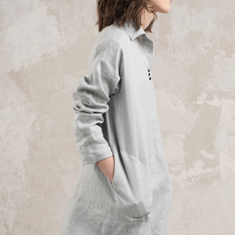 May include: A light grey linen shirt dress with a collared neckline and long sleeves. The dress has a button closure and two pockets.