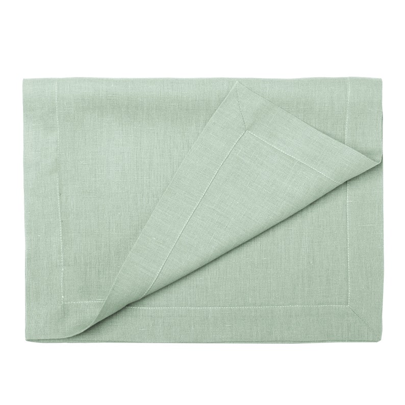 Peut inclure: Un set de table en lin vert clair avec un coin pli&eacute;, mettant en valeur une bordure cousue d&eacute;taill&eacute;e. Le tissu a une texture subtile et la couleur est un vert doux et sourd. Le set de table est rectangulaire et con&ccedil;u pour la salle &agrave; manger.