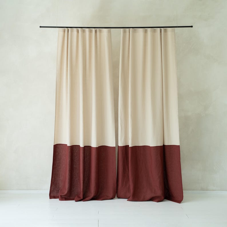 Puede incluir: Cortinas de dos paneles. Cada panel tiene una secci&oacute;n superior crema y una secci&oacute;n inferior burdeos oscuro. Cuelgan de una barra negra, creando un ambiente acogedor y elegante.