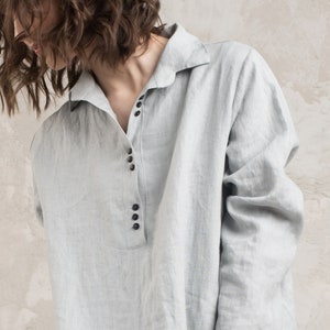 May include: A light blue linen shirt with a collared neckline and a button-up front. The shirt has a relaxed fit and long sleeves.