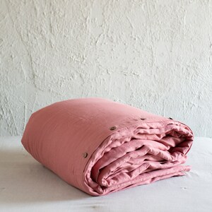 Puede incluir: Una funda n&oacute;rdica de lino rosa doblada con botones de cierre. La funda n&oacute;rdica est&aacute; hecha de un tejido suave y natural, ideal para un sue&ntilde;o c&oacute;modo y acogedor.