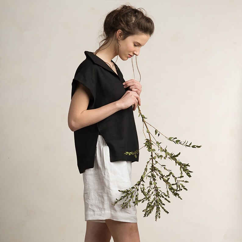 Peut inclure: Une femme portant un haut en lin noir avec un col et un short en lin blanc. Elle tient une branche avec des feuilles vertes.