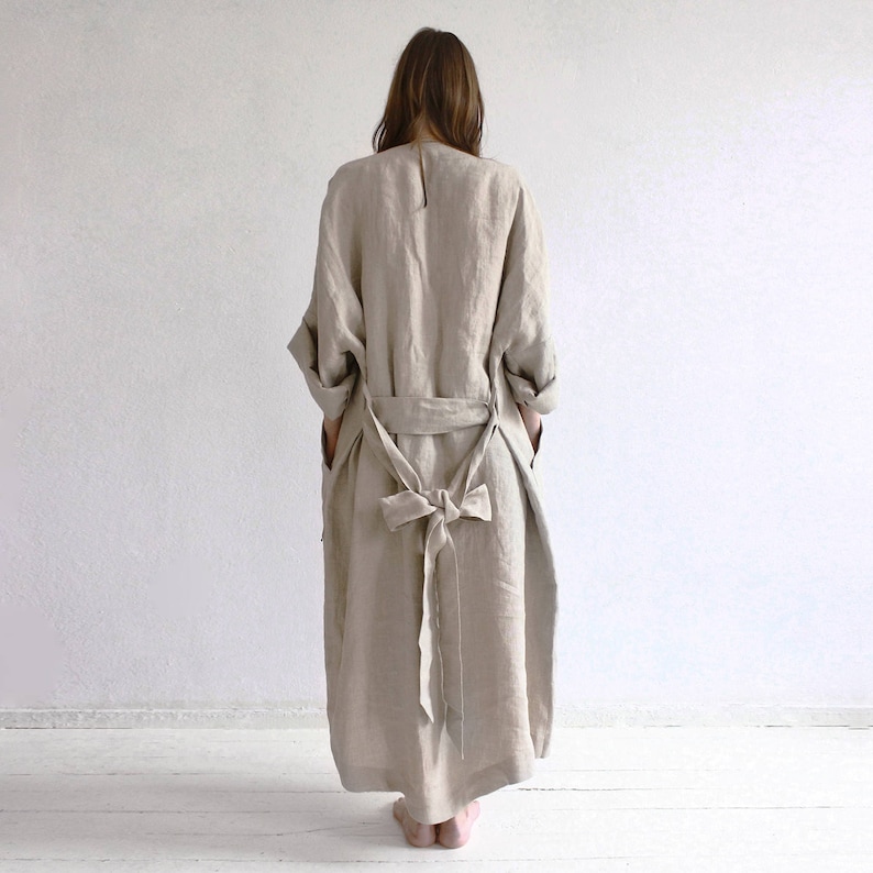 May include: A long, beige linen robe with a self-tie belt. The robe has a relaxed fit and a simple design.