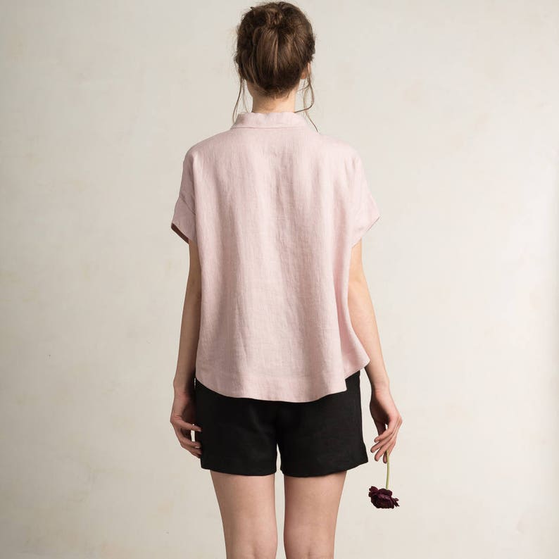 May include: A pink linen shirt with short sleeves and a relaxed fit. The shirt is worn with black shorts.