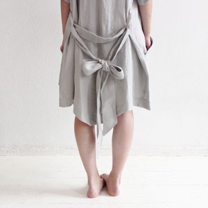 May include: A light grey linen dress with a large bow at the back. The dress is loose fitting and has a relaxed silhouette.