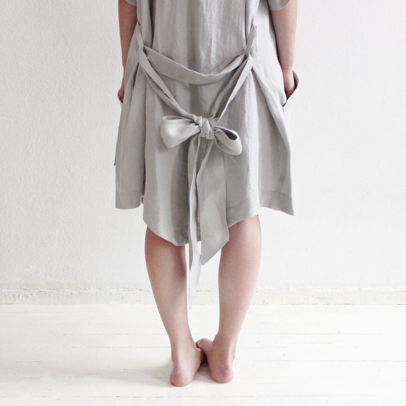 May include: A light grey linen dress with a large bow at the back. The dress is loose fitting and has a relaxed silhouette.