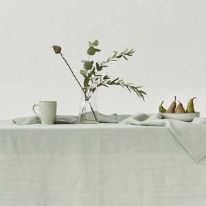 Peut inclure: Une nature morte paisible avec une nappe en lin vert clair. Un vase en verre transparent contient des branches d'eucalyptus. Une tasse en c&eacute;ramique et un bol de poires compl&egrave;tent la sc&egrave;ne. L'ensemble &eacute;voque le calme et la simplicit&eacute;, id&eacute;al pour la d&eacute;coration int&eacute;rieure.