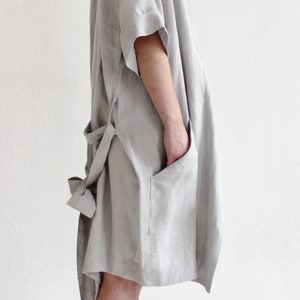 May include: A light grey linen robe with a tie belt and a patch pocket. The robe has a relaxed fit and is made of a soft, breathable fabric.