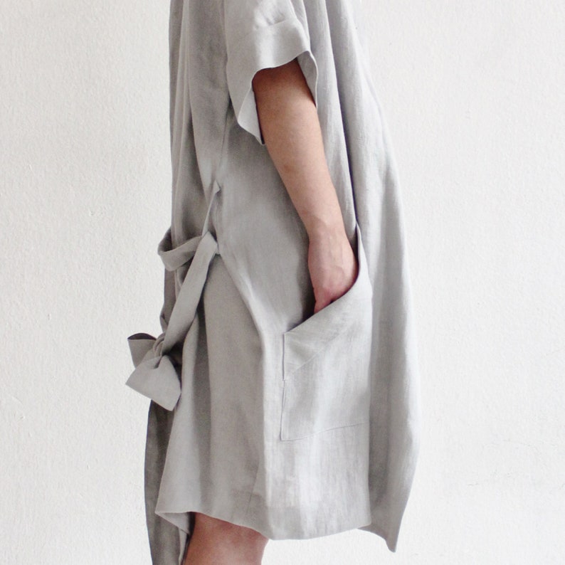 May include: A light grey linen robe with a tie belt and a patch pocket. The robe has a relaxed fit and is made of a soft, breathable fabric.