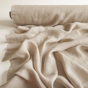 May include: A roll of natural linen fabric in a light beige color. The fabric is soft and has a slightly textured surface. It is folded and draped in a way that shows its texture and drape.