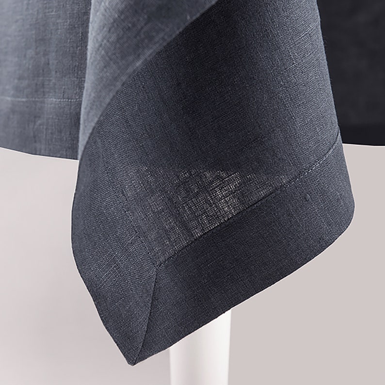 May include: Close-up of a dark gray linen tablecloth with a folded corner. The fabric has a subtle texture and a slightly frayed edge.