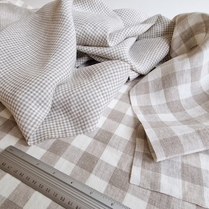 Puede incluir: Dos piezas de tela de lino beige con un patrón de cuadros blancos. La tela está doblada y dispuesta sobre una superficie blanca. Una regla es visible en la esquina inferior izquierda de la imagen.
