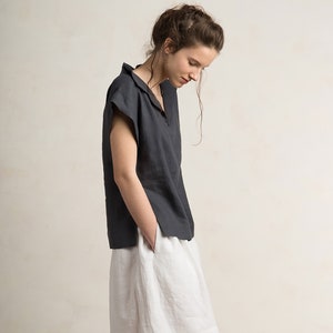May include: A woman wearing a charcoal gray linen top with a v-neck and short sleeves. She is also wearing a white linen skirt.