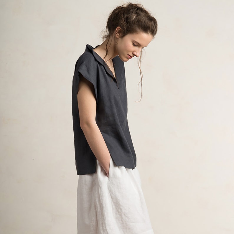 May include: A woman wearing a charcoal gray linen top with a v-neck and short sleeves. She is also wearing a white linen skirt.