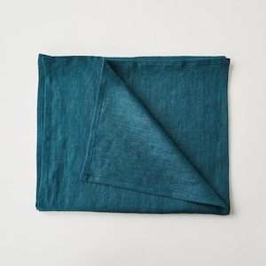 May include: A folded teal blue linen tablecloth. The tablecloth is made of a soft, textured fabric.