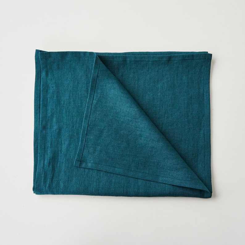 May include: A folded teal blue linen tablecloth. The tablecloth is made of a soft, textured fabric.