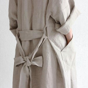 May include: A long, light brown linen robe with a tie belt and a large bow at the back. The robe has a large pocket on the side.