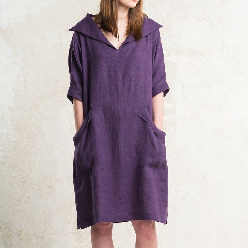 May include: A purple linen dress with a wide collar and two large pockets. The dress has a relaxed fit and a knee-length hem.