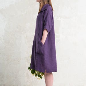 May include: A purple linen dress with a collared neckline and a single patch pocket on the left side. The dress has a relaxed fit and falls to the mid-thigh.
