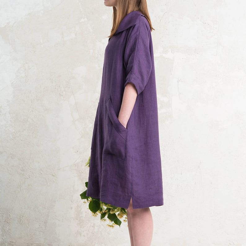 May include: A purple linen dress with a collared neckline and a single patch pocket on the left side. The dress has a relaxed fit and falls to the mid-thigh.