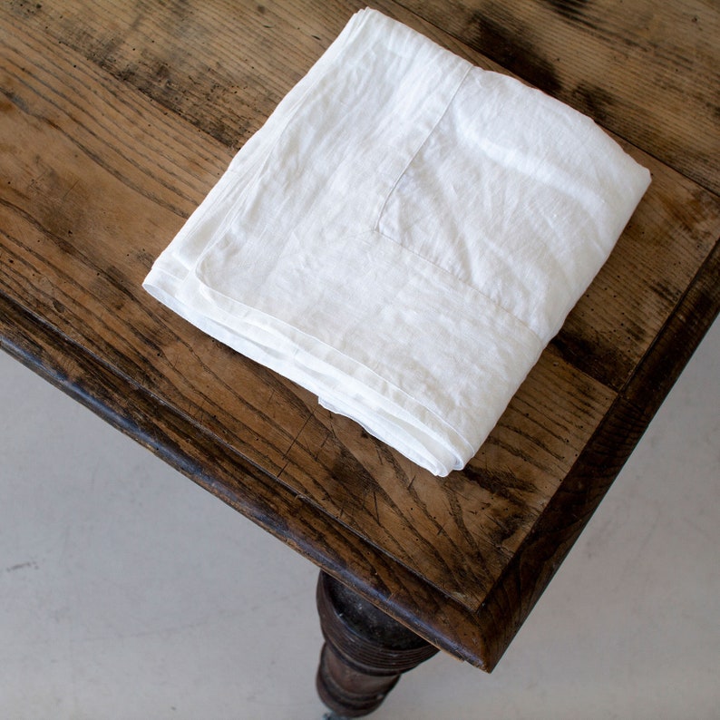 May include: A white linen tablecloth folded on a wooden table with a dark brown stain.