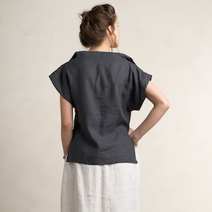 May include: A dark gray linen top with short sleeves and a relaxed fit. The top has a scoop neckline and a slightly cropped hem.