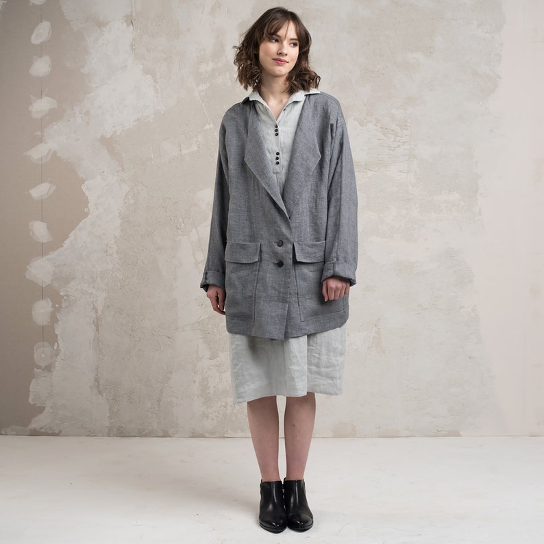 May include: A grey linen blazer with a long, relaxed fit and a single button closure. The blazer has two large pockets on the front and a slightly oversized collar.