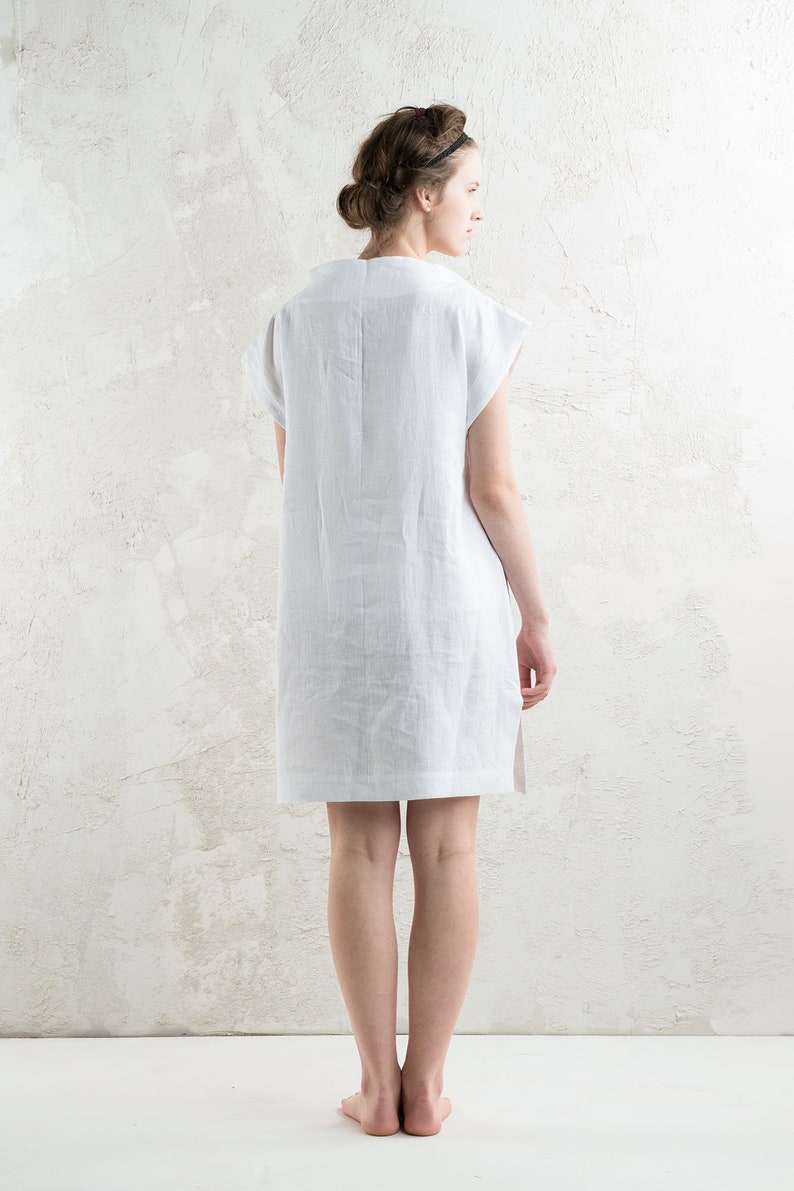 May include: A white linen dress with short sleeves and a straight silhouette. The dress is shown from the back, with the model standing on a white background.