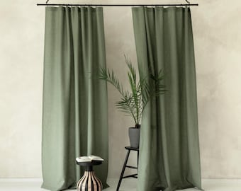 May include: Two floor-length sage green curtains hang from a black metal rod suspended by chains. A small black stool holds an open book, and a potted palm plant sits on a taller black stool between the two fabric panels.