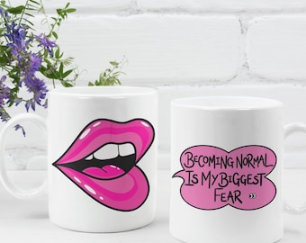 May include: Two white ceramic mugs. One mug features a pink lip design, and the other has the text "Becoming Normal Is My Biggest Fear" in a pink speech bubble. A white vase with purple flowers is also in the image.
