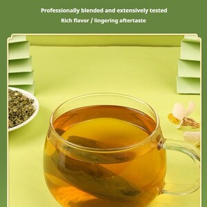 May include: A clear glass mug filled with amber-colored tea, with a tea bag visible inside. The image includes text that reads "Meticulously crafted to exceed your expectations". A small white dish of loose tea leaves is in the background.