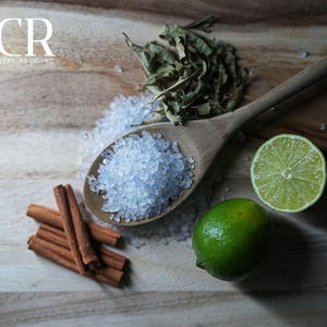 May include: A wooden spoon filled with blue-tinted salt sits on a wooden surface, next to a lime, cinnamon sticks, and dried herbs. The image includes the text "BCR BLUE CRYSTAL ROCK INC."