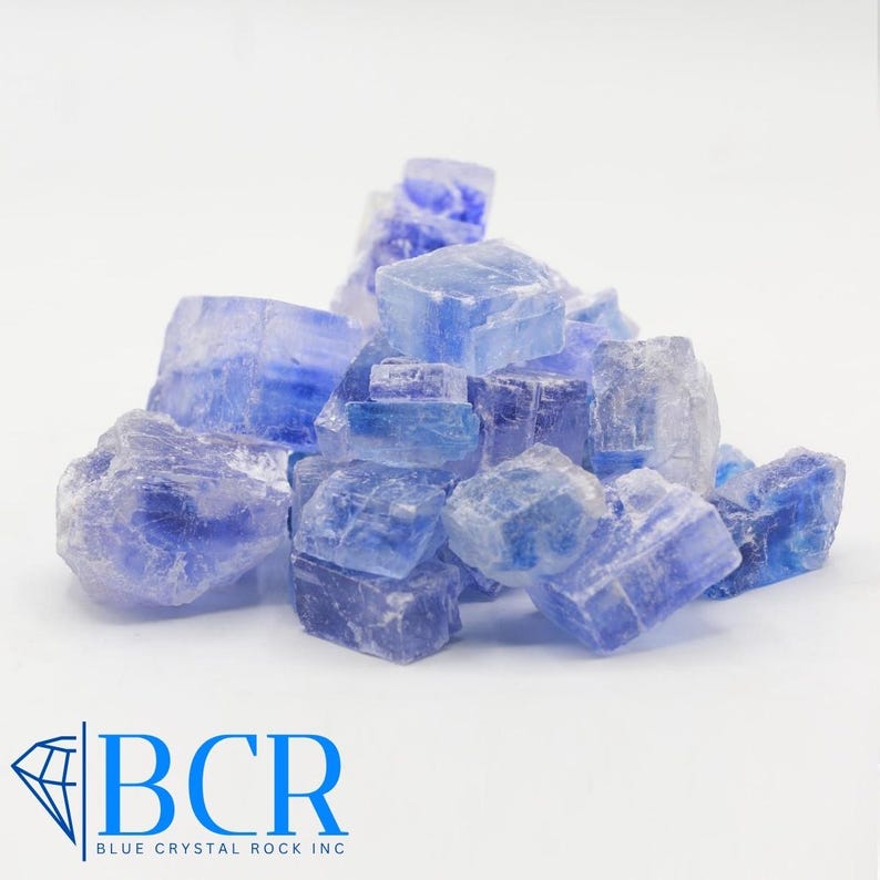 May include: A pile of blue crystals with a crystalline structure. The crystals vary in size and shape, with a range of blue hues. The logo "BCR BLUE CRYSTAL ROCK INC" is in the lower left corner.