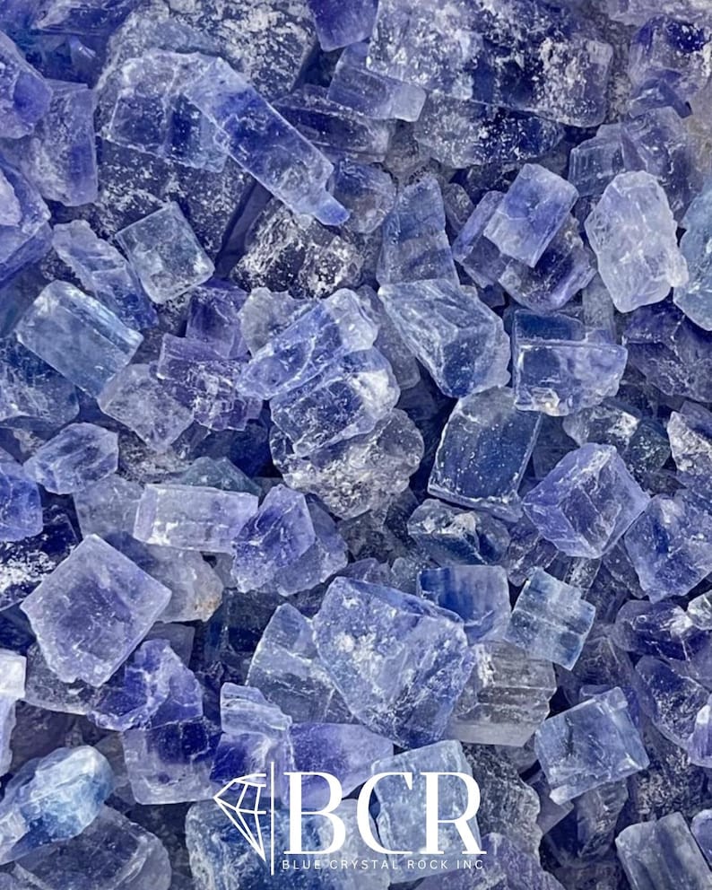 May include: A close-up shot of a collection of blue crystals. The crystals vary in size and shape, with a mix of light and dark blue hues. The image includes the text "BCR BLUE CRYSTAL ROCK INC."